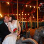 A bride and groom kiss on the Zoo carousel at night.
