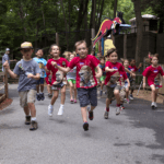 A group of kids wearing Summer Safari shirts run through the zoo.