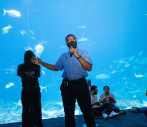 An Exhibit Interpreter informs guests in front of a large aquarium window. 