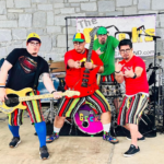 The band The Geeks poses in front of a banner with their instruments