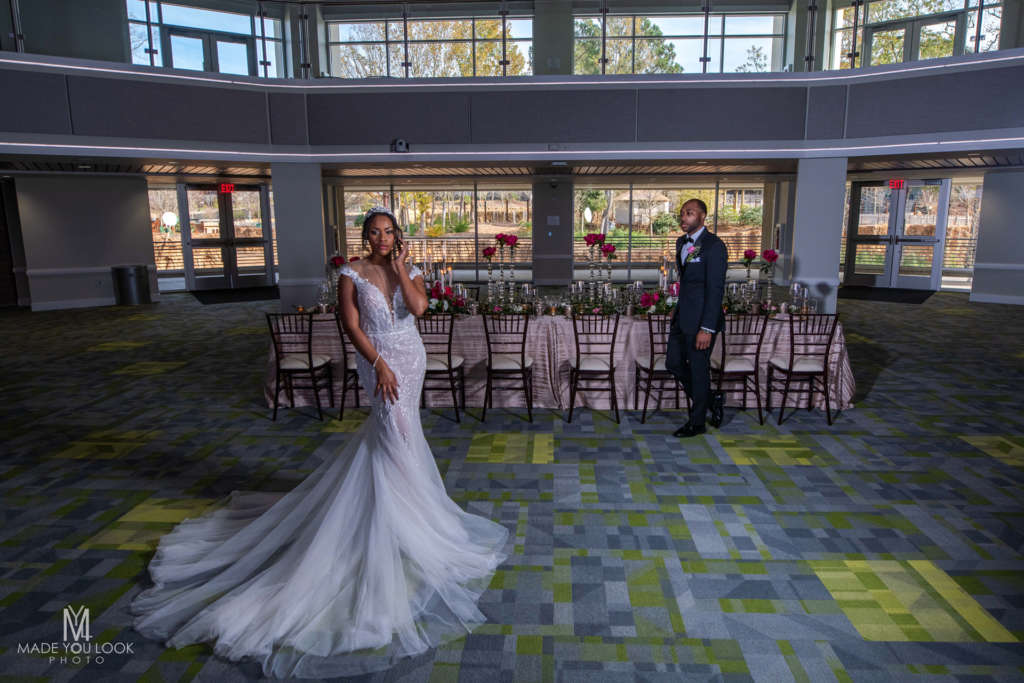 A couple dressed in formal attire pose in front of a set table in the Carlos Ballroom.