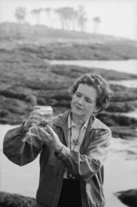 Rachel Carson stands outdoors examining a jar.