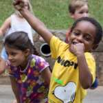 A group of school children play and dance outside.