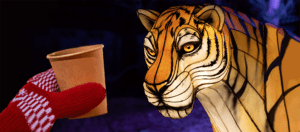 A hand wearing a red woven glove holds a paper cup in front of a Chinese lantern of a cheetah.