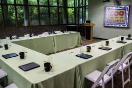Tables set-up in a u-shape with folders and coffee mugs in a meeting room.