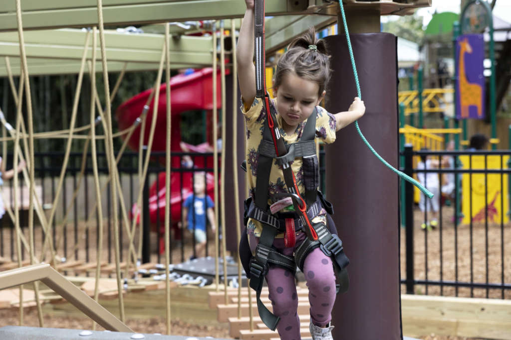 A small child navigates the ropes of Treetop Tykes Trail, a new aerial ropes course for children.