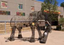 A life size statue of an elephant made of open wire stands in front a building decorated in African inspired patterns.